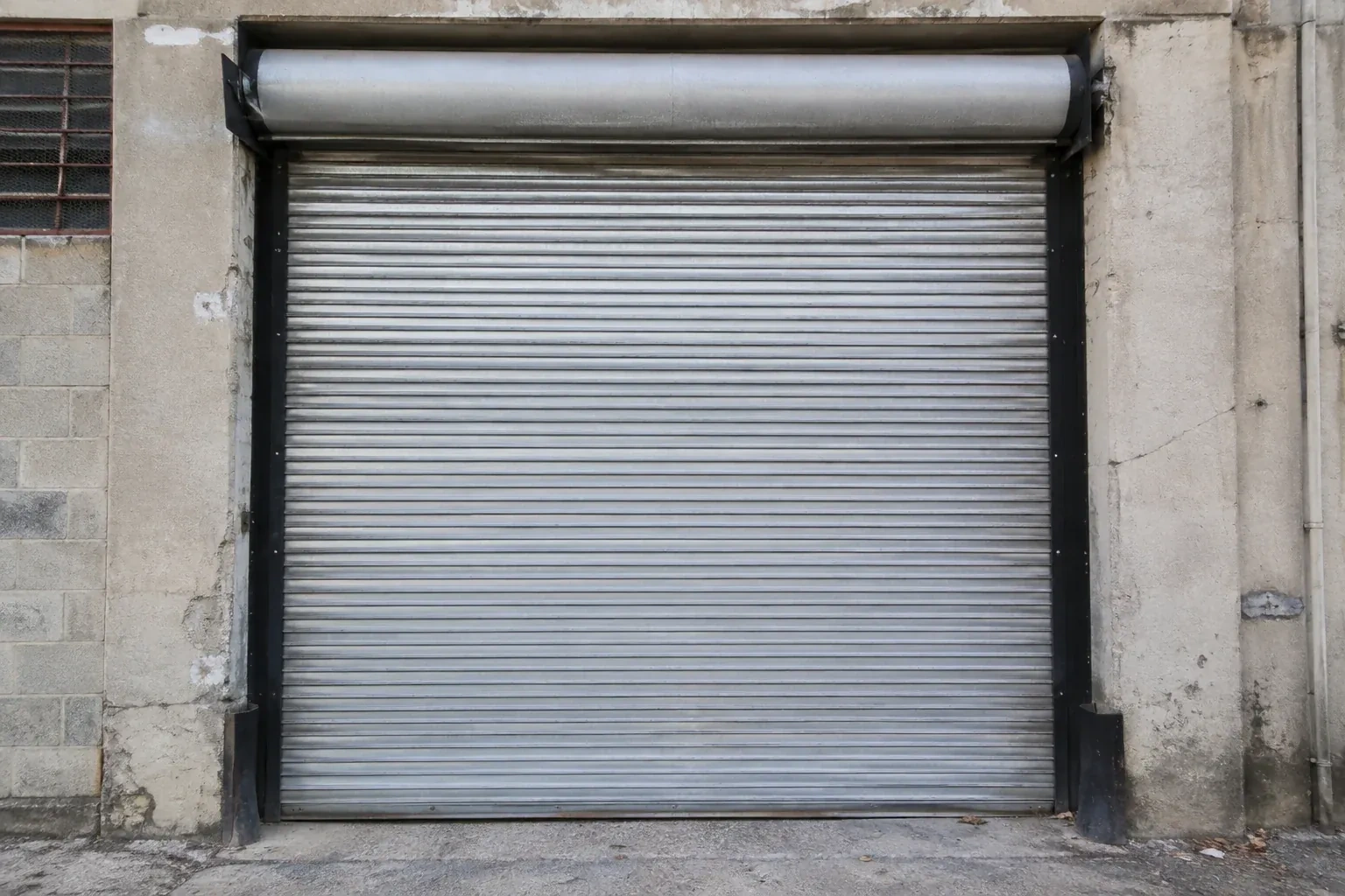Closed metal rolling shutter in a weathered warehouse opening. — Commercial Rolling Door Repair, Oakville