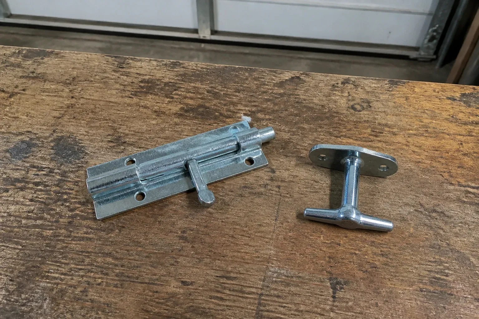 Detached slide bolt and T-handle on a wooden garage workbench. — Garage Door Manual Lock Repair, Oakville