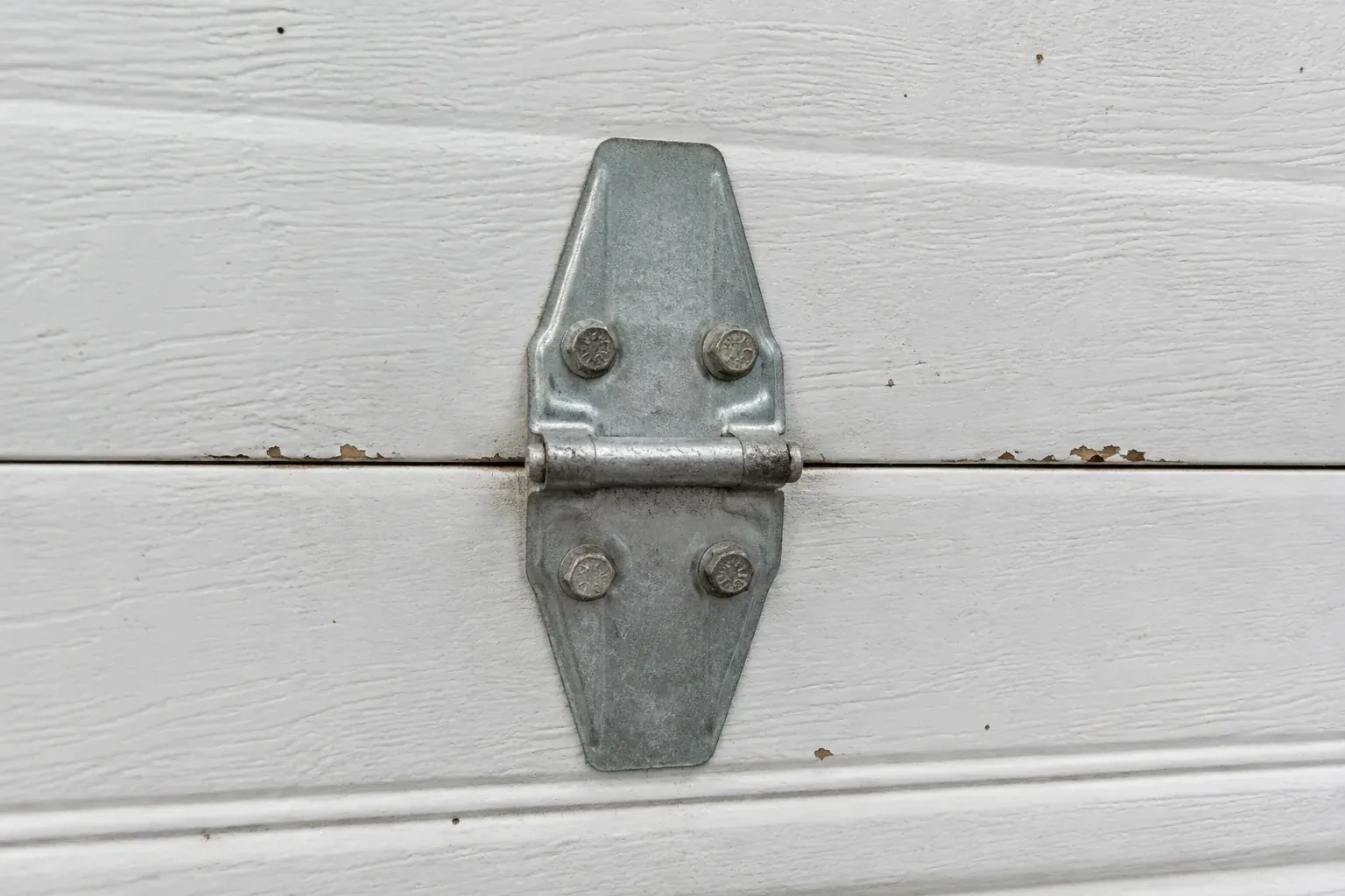 Metal center hinge across a seam in a white sectional garage door. — Garage Door Hinge Replacement, Oakville